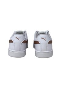 Para białych sneakersów Puma z brązowym logo na pięcie i brązowym paskiem po bokach, widocznych od tyłu na białym tle.