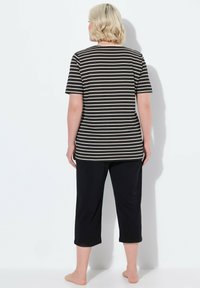 Top corto de manga corta a rayas negras y crema combinado con pantalones negros cortos, mostrando un ajuste relajado y una tela suave.