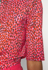 Krátký rukáv top v živé červené barvě s růžovým a černým puntíkovaným vzorem. Měkká tkanina s mírnou elasticitou a volným střihem.