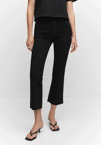 Nainen, joka käyttää mustia korkeavyötäröisiä cropped flare -farkkuja, joissa on repsottavat helmat, yhdistettynä mustiin korkokenkiin ja mustaan lyhytvartiseen toppiin.