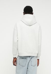 Sudadera con capucha gris de corte relajado, hecha de una tela suave. Presenta puños y dobladillo acanalados, con un diseño sencillo y sin patrones visibles.