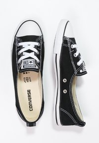 Baskets Converse en toile noire avec semelles en caoutchouc blanches, design classique à lacets, surpiqûres contrastées et détails de marque en noir et blanc.