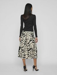 Haut noir à manches longues associé à une jupe plissée beige avec des rayures noires zèbre ; le mannequin porte des chaussures à talons noires avec des brides de cheville.