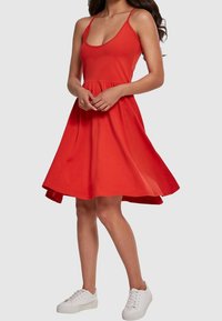 Robe sans manches rouge avec un corsage ajusté et une jupe évasée, fabriquée en coton. Présente un décolleté en forme de cœur et arrive juste au-dessus des genoux.