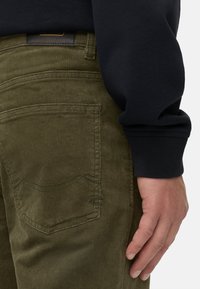 Dunkelgrüne Cordhosen mit einer strukturierten Oberfläche und dünnem Rippmuster. Mit Gesäßtaschen und einem Lederschild am Bund.