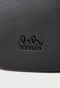 Juodas odinis paviršius su iškilniu logotipu "lala BERLIN" blizgia juoda spalva, lygia tekstūra su šiek tiek smulkia tekstūra.