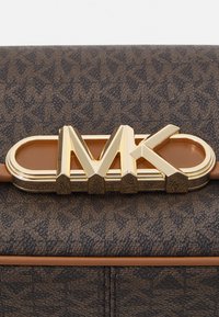 Sac à main en cuir marron texturé, mettant en avant un fermoir en métal doré emblématique de MK et des accents beiges, soulignant le design structuré et l'artisanat détaillé.