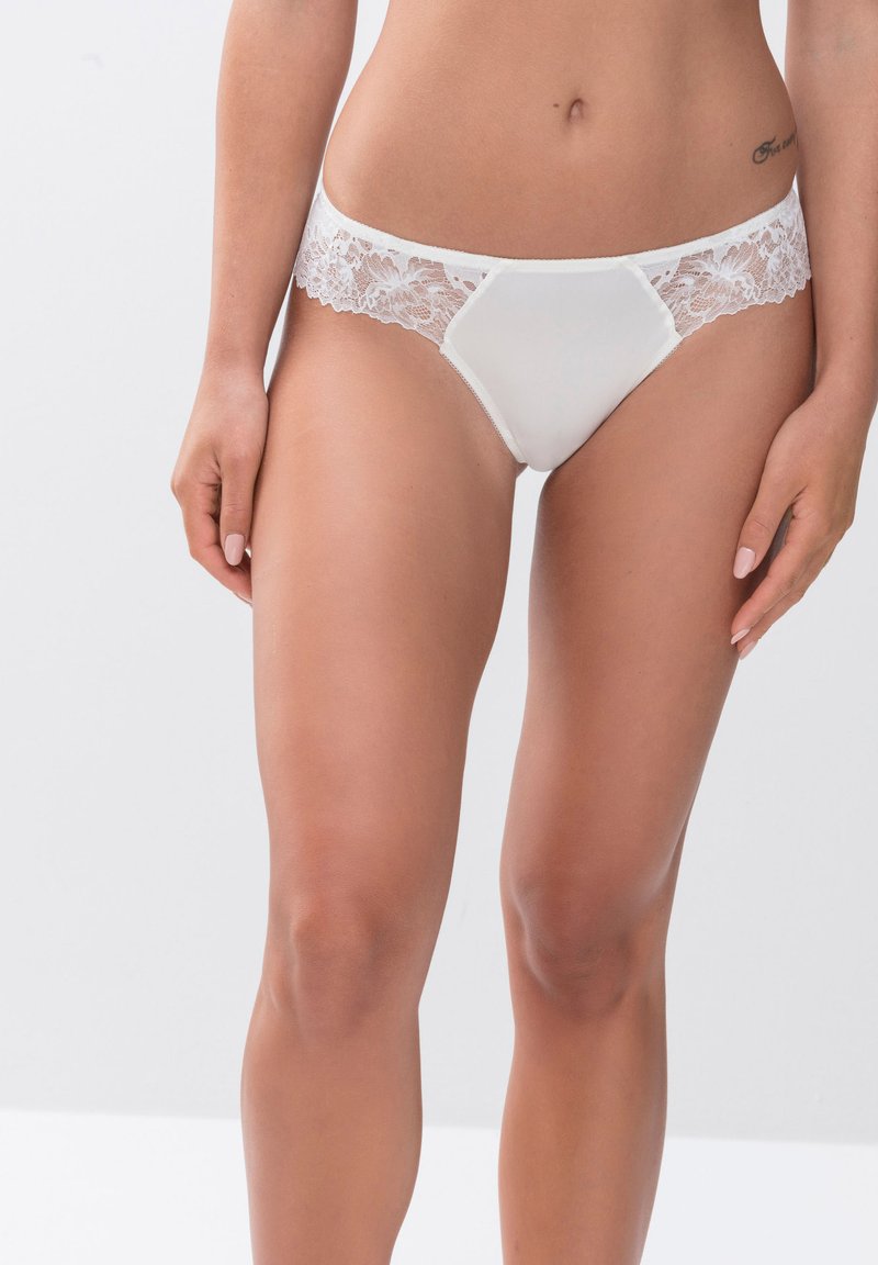 Witte slip met kant, voorzien van een satijnachtige voorkant, zachte textuur en een driehoekige vorm met decoratieve stiksels langs de randen.