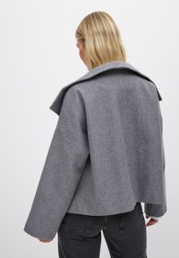 Grå ullblandad jacka med en stor krage, vida ärmar och en kortad design. Har en strukturerad yta och minimalistisk stil.