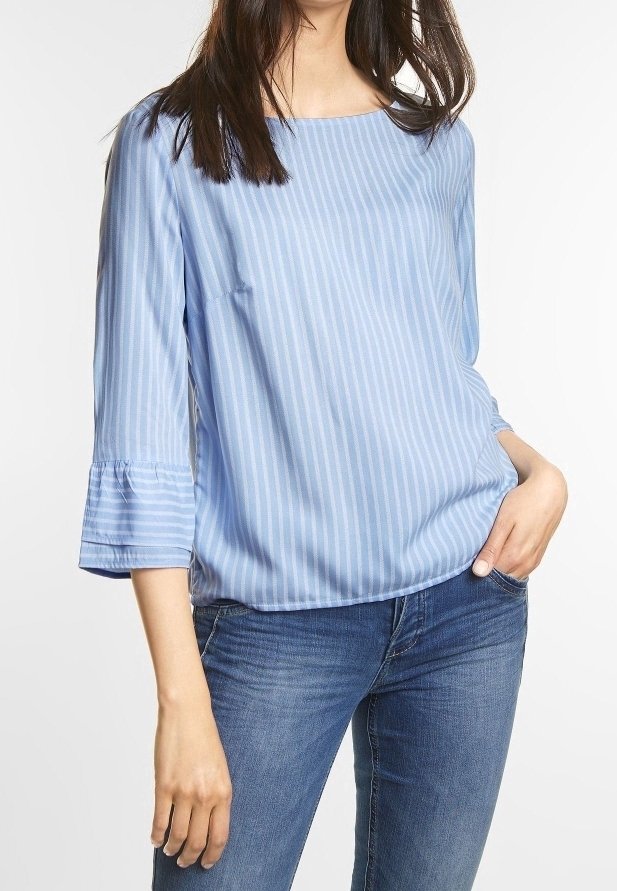 Blouse rayée bleu clair avec une coupe ample, un col rond et des manches en cloche trois-quarts, associée à un jean noir. Texture douce.