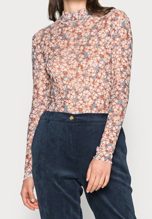 Langærmet top med høj hals i gennemsigtigt stof, prydet med et blomstermønster i nuancer af fersken, blå og hvid. Kombineret med mørke fløjlsbukser.