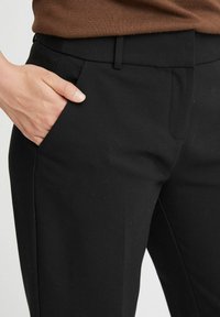 Czarne spodnie wykonane z gładkiego materiału, z przednimi kieszeniami, dopasowanym krojem i płaskim pasem, prezentujące czysty i minimalistyczny design.