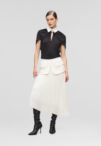 Black bodysuit with white collar, keyhole detail, and attached cape; white pleated skirt with pockets; black pointed-toe heeled boots.