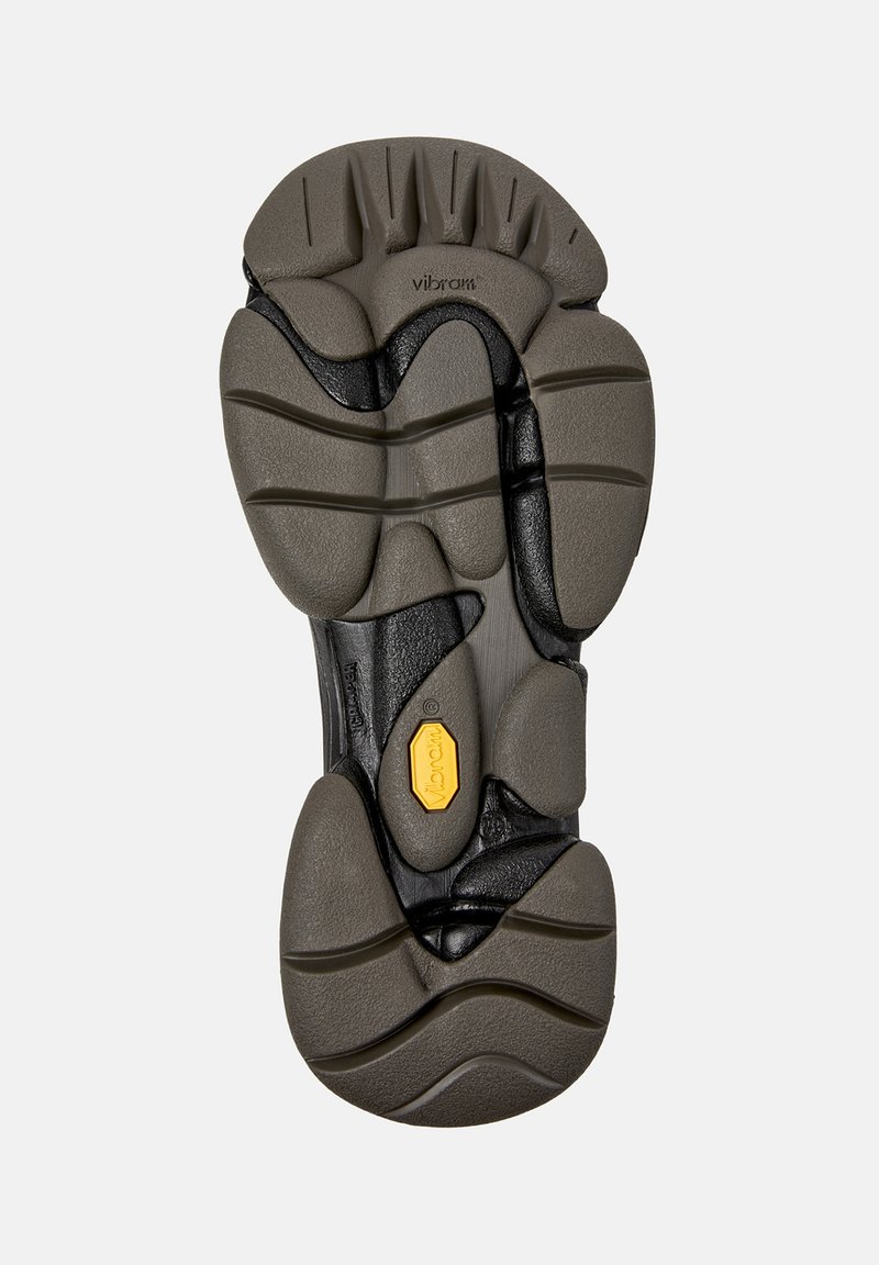 Sohle eines Vibram-Schuhs mit strukturiertem grauem und schwarzem Gummi-Grip und dem gelben Vibram-Logo in der Mitte.