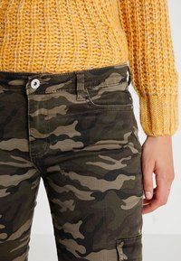Pantalons en coton à motif camouflage dans des teintes de vert et de marron avec une fermeture à boutonnage, dotés de poches latérales et d'une silhouette ajustée.