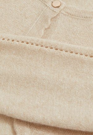 Tessuto lavorato a maglia beige chiaro con un leggero luccichio, dotato di scollo rotondo e bottone decorativo, texture fine e dettagli di cucitura aperta.