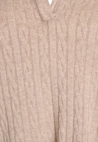 Bež pleteni pullover s V-izrezom, teksturiranim kabel uzorkom i mekanom tkaninom. Naglašava vertikalne linije i suptilne varijacije u tonu.