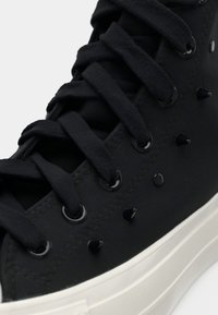 Schwarze Canvas High-Top-Sneaker mit schwarzen Schnürsenkeln, glänzenden Ösen und Stachelakzenten im Obermaterial. Weiße Gummisohle mit strukturierten Details.