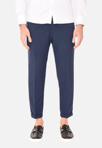 Pantaloni blu navy con un design slim fit, orli arricciati, texture liscia e due tasche frontali, abbinati a scarpe nere slip-on.