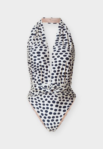 Biely plavkový overal s halterovým výstrihom na krk, čierne bodky, hlboký výstrih do písmena V, zdobený pás a uzlík vpredu.