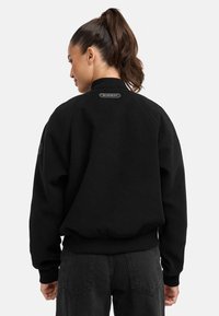 Black sweatshirt with a high neckline, ribbed cuffs, and hem. Features a logo patch at the collar and textured fabric. Back view shown.