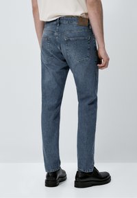 Blå denimjeans med rak benklipp, bakfickor och läderlapp på midjan. Avslutade med subtila blekningar och kontrastsömmar.