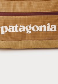 Close-up of a yellow and brown textured fabric bag with a maroon zipper and white "patagonia" logo printed across the surface.