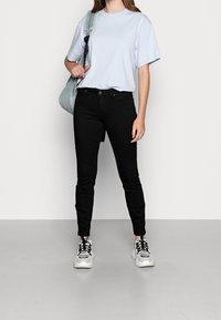 Camiseta de algodón azul claro, corte relajado. Vaqueros negros ajustados, textura suave. Zapatillas blancas y negras con suelas gruesas. Bolsa de hombro gris.