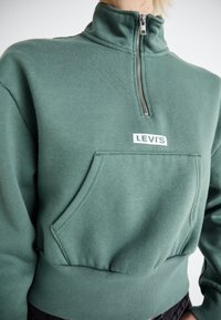 Felpa verde con zip realizzata in cotone misto, con colletto alto, tasca a marsupio e logo bianco di Levi's sul petto. Texture morbida.