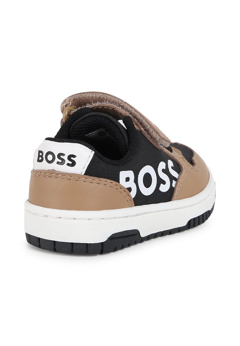 Zapatilla negra y marrón con una correa de velcro, que cuenta con una suela blanca gruesa y un gran logo "BOSS" en el costado. Acabados en cuero texturizado.