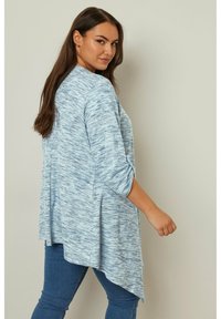 Ljusblå, texturerad tröja med lång ärm och asymmetrisk nederkant, uppvikt ärm, i kombination med mörkblå skinny jeans.