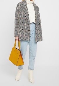 Blazer i houndstooth-mønster, hvid turtleneck, lyseblå jeans, gul struktureret håndtaske og cremefarvede ankelstøvler.