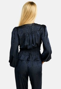 Tumesinine satiinilaadne pluus, millel on õhukesed voldilised varrukad, kummiga treitud vöökoht ja peen tekstuuriga muster. Allosas on peplumi detailid.