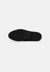 Suela de zapato de goma negra con un patrón de diseño profundo, que presenta bordes redondeados y una superficie texturizada para ofrecer agarre y durabilidad.