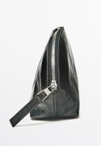 Sort pung i imiteret læder med trekantet form, sølvfarvet lynlås og håndledsrem. Glat tekstur med en blank overflade.