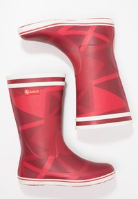Bottes de pluie en caoutchouc rouge avec des motifs géométriques, rayures blanches en haut et sur la semelle, texture lisse et logo Aigle sur le côté.