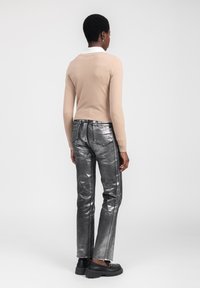 Beige Langarmpullover mit einem weißen Kragen, kombiniert mit hoch taillierten, metallisch silbernen Hosen und schwarzen Schuhen mit dicker Sohle.