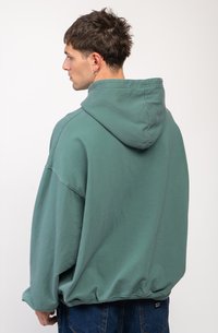Felpa verde oversize in morbido tessuto, con cappuccio ampio e orlo a coste. Vista da dietro, con una vestibilità morbida.