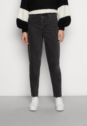 High-waisted, slim-fit jeans in dark grey denim with a button fly. Paired with white sneakers, featuring a textured black and white knit sweater.