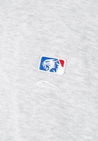 Besticktes Logo eines brüllenden Tigerkopfs in Blau, Weiß und Rot auf hellgrauem Stoff mit einem dezenten weißen Schwung darunter.