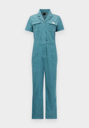 Teal corduroy jumpsuit with short sleeves, two chest pockets, a fitted waist, and straight legs, featuring a branded patch near the pocket.