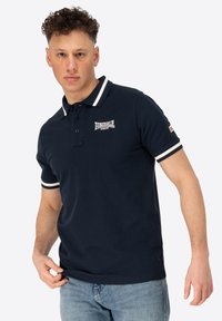 Marine polo t-shirt med hvidstribede krave og ærmeaccenter, med broderet logo på brystet, lavet af blødt bomuldsstof.