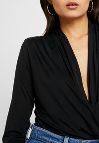 Schwarzer Langarm-Body mit tiefem V-Ausschnitt, aus glattem Material gefertigt, kombiniert mit hoch taillierten Jeans.