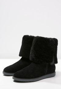 Stivali alla caviglia in camoscio nero con morbido risvolto in pelliccia. Punta arrotondata e suola piatta in gomma con leggera scanalatura. Design minimalista, stile versatile.