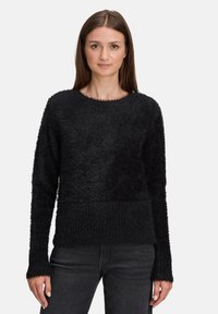 Czarny sweter o puszystej fakturze, z okrągłym dekoltem i prążkowanym obszyciem na dole. Długie rękawy zakończone lekko rozszerzanymi ściągaczami, noszony z ciemnymi jeansami.