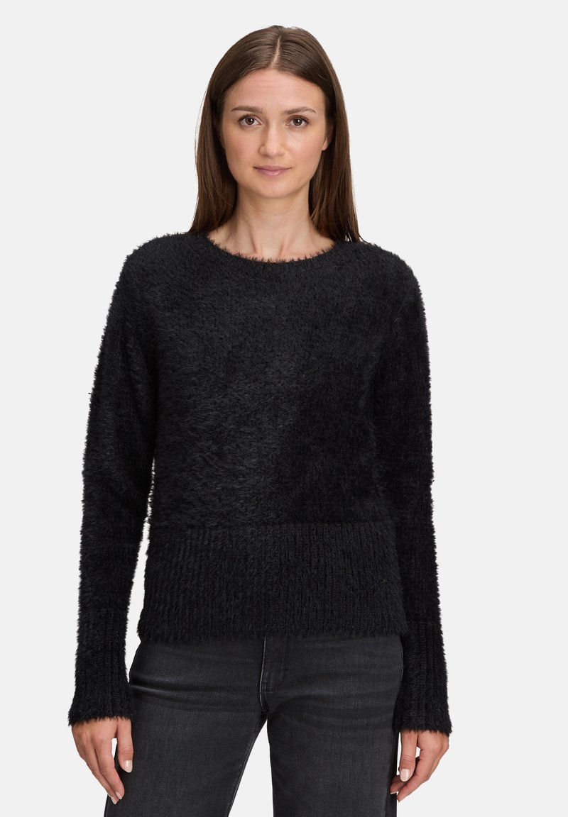 Czarny sweter o puszystej fakturze, z okrągłym dekoltem i prążkowanym obszyciem na dole. Długie rękawy zakończone lekko rozszerzanymi ściągaczami, noszony z ciemnymi jeansami.