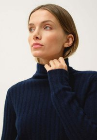 Granatowy sweter z długim rękawem i prążkowanym kołnierzem. Ma dzianinową strukturę oraz dopasowany krój, a także wysoki kołnierz i miękki materiał.