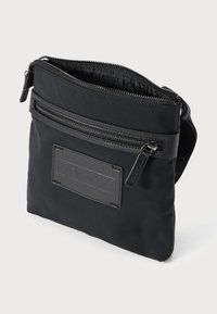 Small black crossbody bag with front zip pocket, top zip closure, and Armani Exchange logo patch on front.