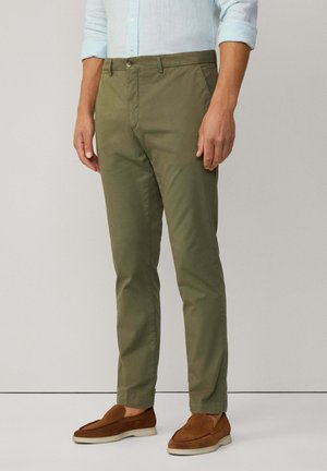 Chinos vert olive en coton avec une texture lisse, design slim fit et une fermeture à bouton à l'avant. Complétés par des chaussures marron à enfiler.