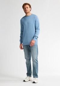 Lichtblauwe gebreide trui met een ronde hals, lange mouwen en geribde manchetten, gecombineerd met lichtblauwe jeans en witte sneakers.